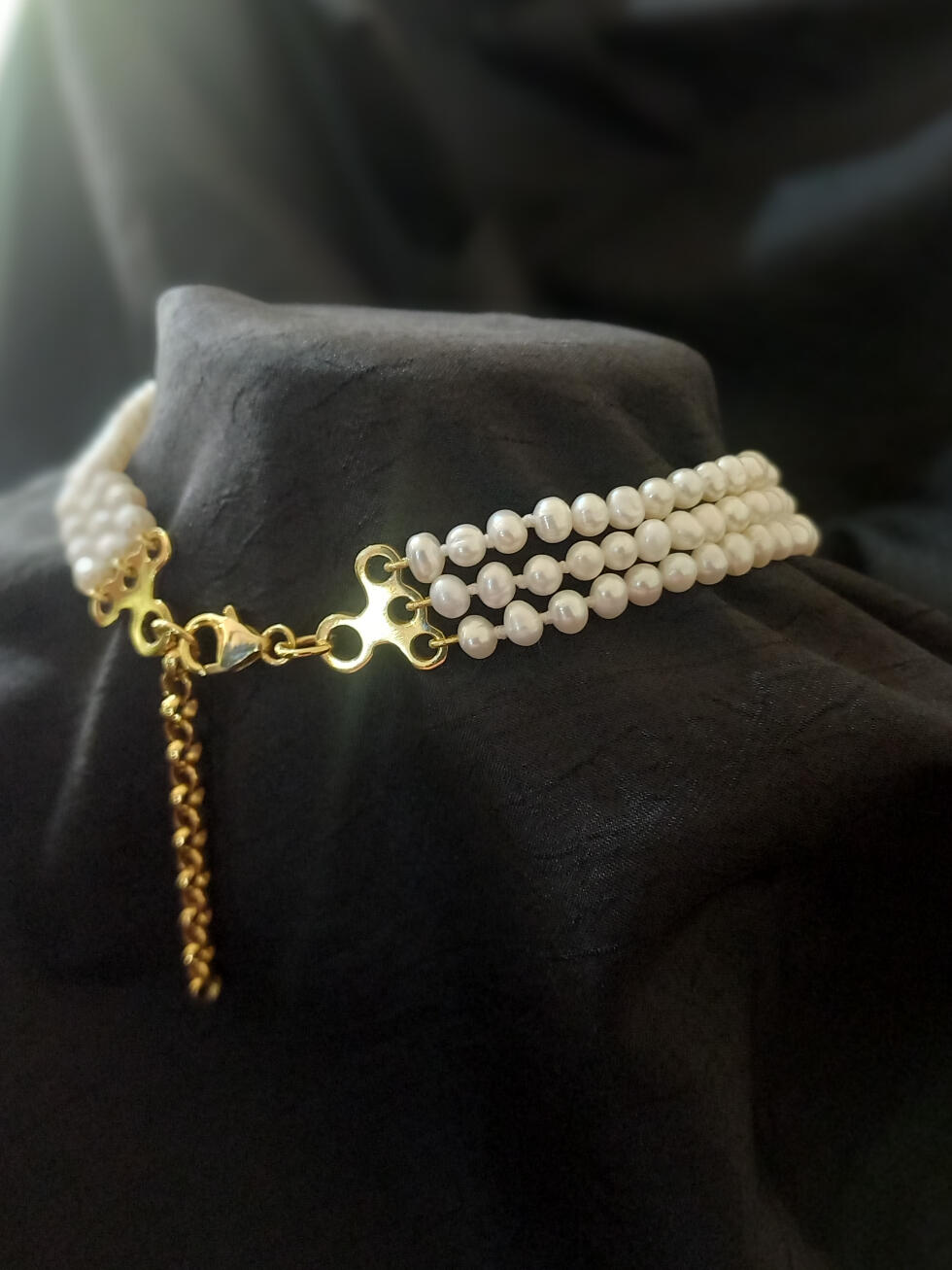 Rear view of a three-strand freshwater pearl choker on gold-plated findings with gold French wire, lobster clasp, and chain to adjust length.